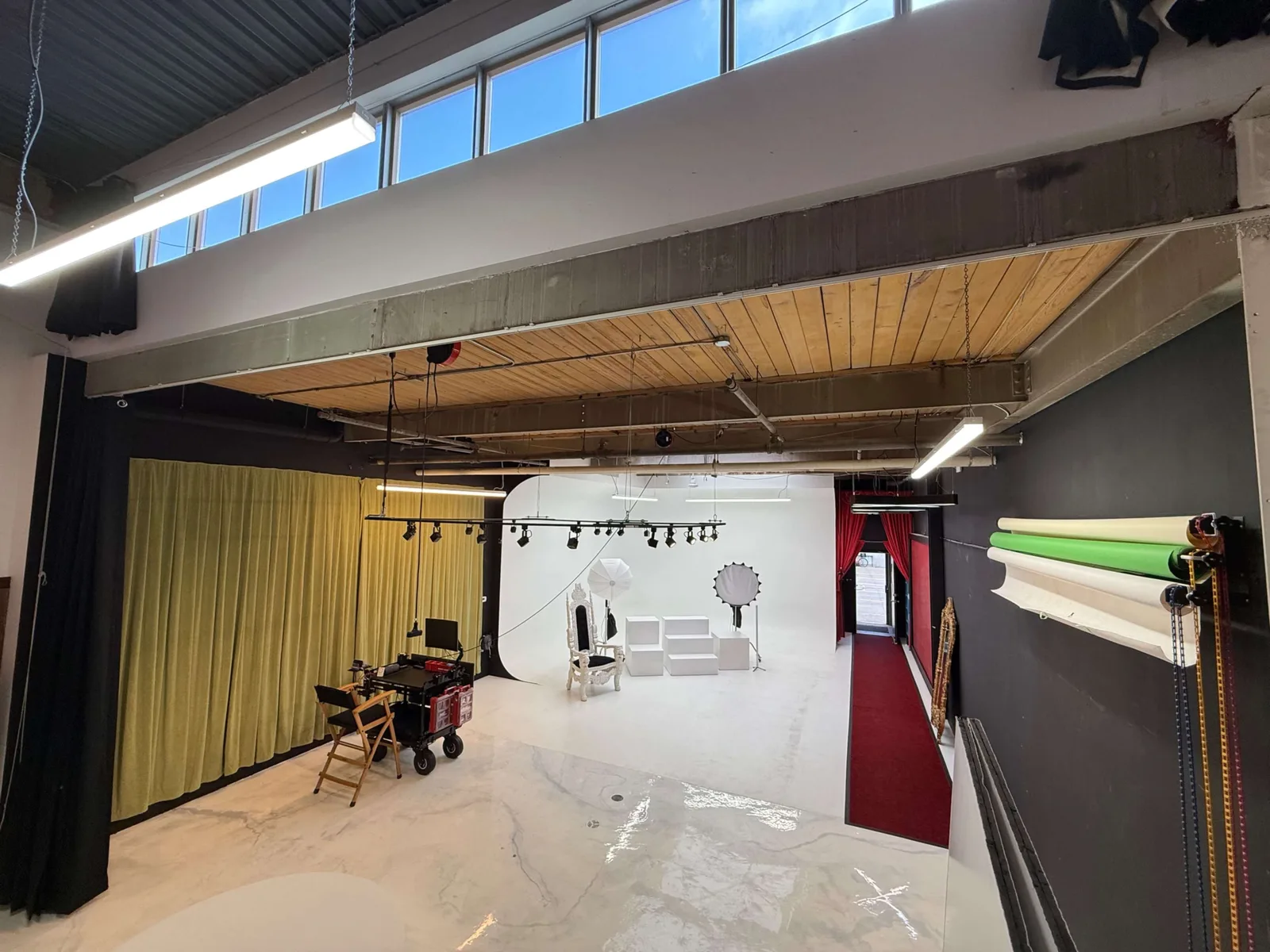 Inside RVXSTUDIO in Toronto: a white cyclorama wall, lights on a ceiling track, a softbox and a beauty dish on stands, backdrop rolls racked on the far wall, an equipment cart, and a red-carpet entrance at the back.